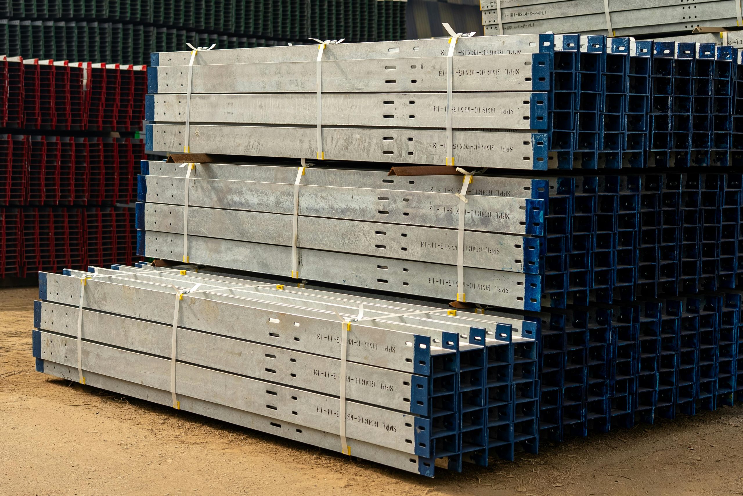 Home Neatly stacked metal beams in an outdoor industrial yard under daylight.