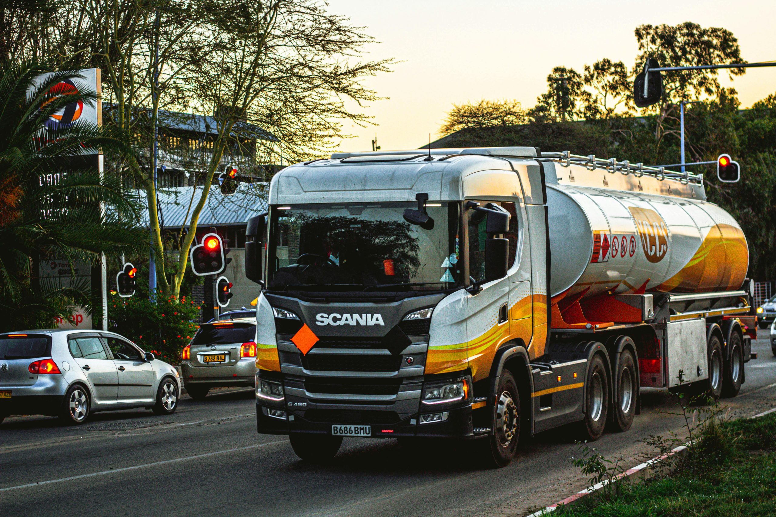 Home Fuel tanker truck navigating city roads during daytime with traffic signals and surrounding vehicles.