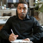 A professional adult man taking notes in a modern office setting, creating a focused atmosphere.