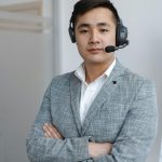 Asian male call center operator wearing a gray suit with a headset, providing customer service support.